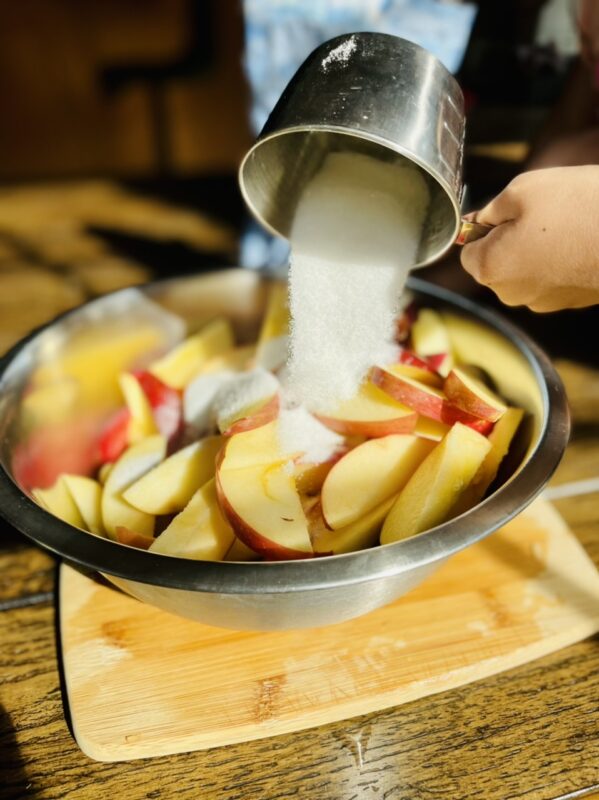 pouring sugar into a bowl of apples